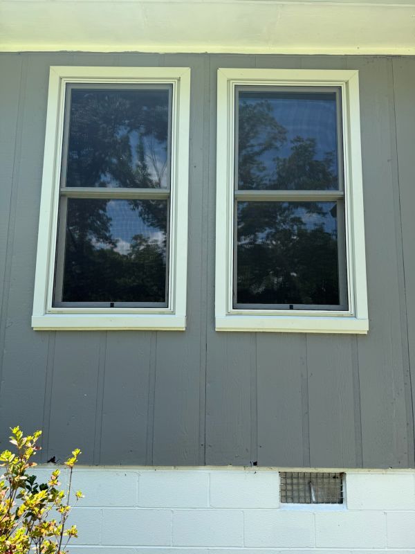 Two new double-hung windows with cream-colored trim on a gray-sided home.
